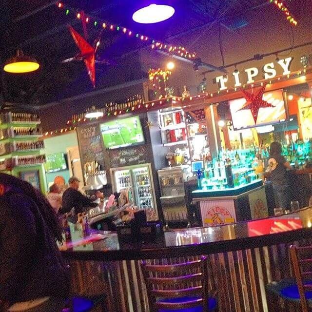 Colorful nightclub bar interior with neon lights, a TV, and patrons seated at the counter