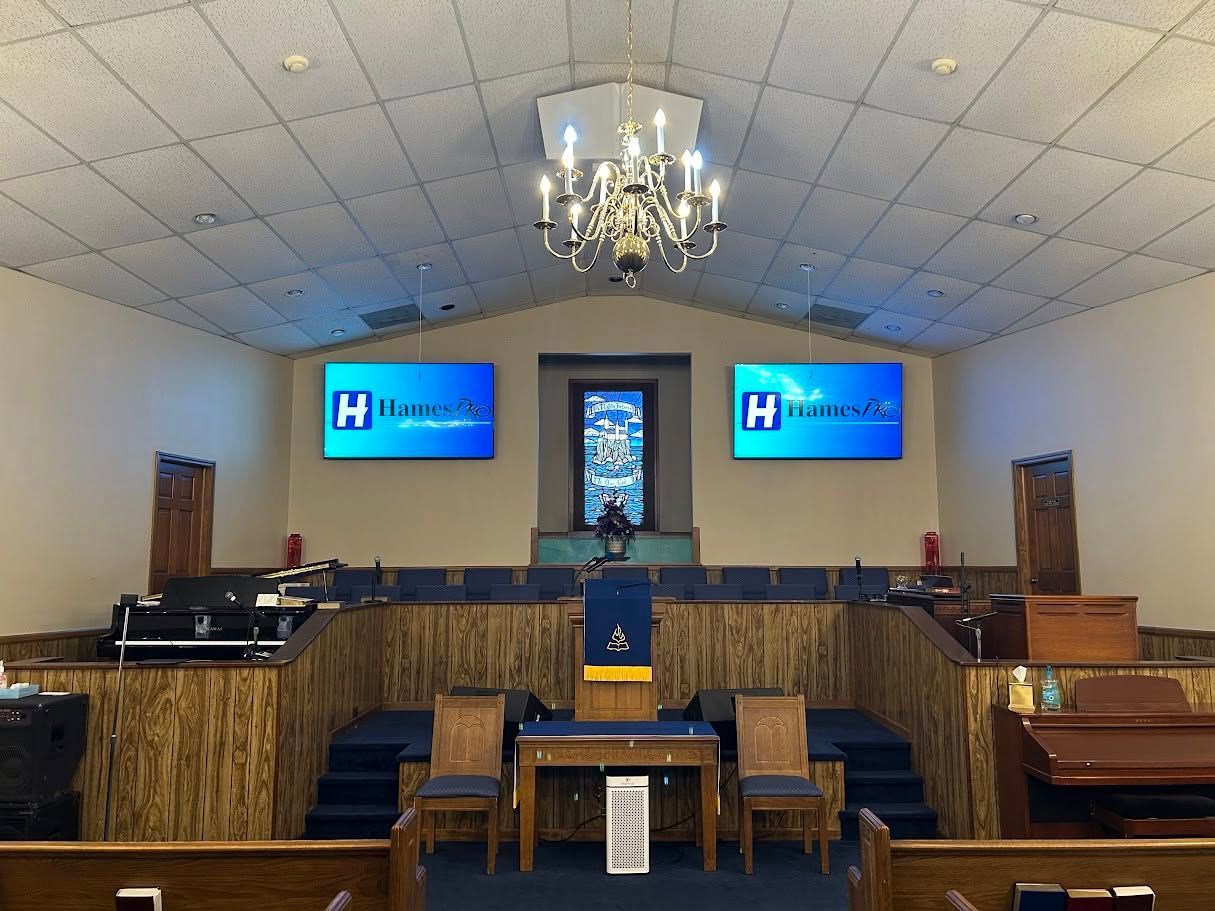 Church sanctuary with pulpit, choir seats, chandelier, and two screens displaying a logo