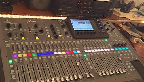 Sound mixing console with rows of sliders, lit buttons, and a central display in a studio.