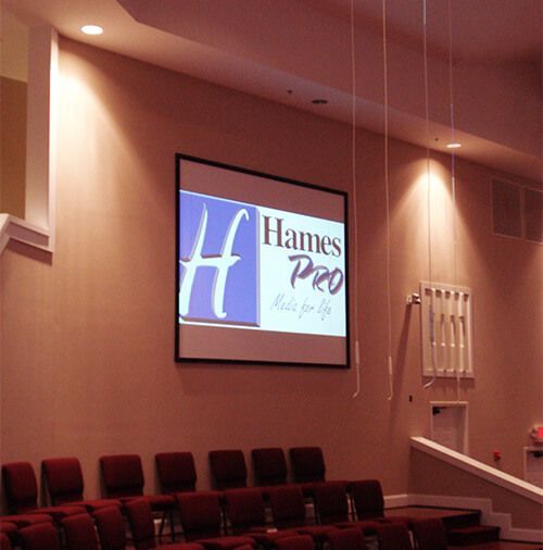 Conference room with a projected “Hames Pro” logo on a screen above rows of red chairs.