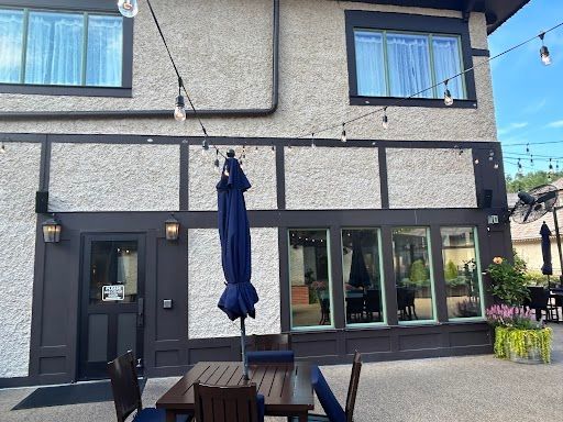 Exterior of a two-story building with dark trim, large windows, patio tables, and a closed navy umbrella.