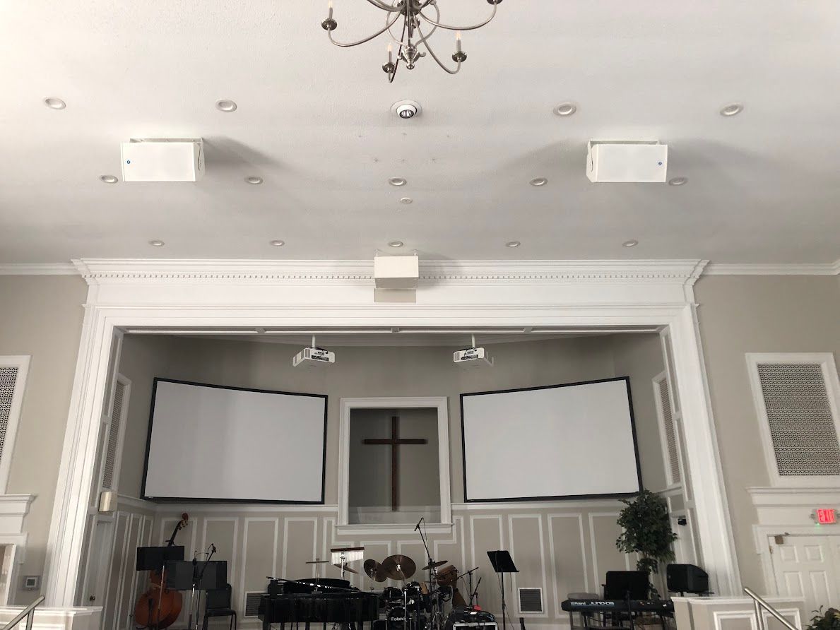 Interior of a hall with a high ceiling, chandelier, projector screens, and a small stage area