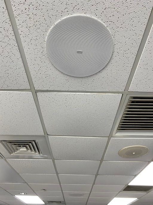 Ceiling tiles with round white speaker and vents in an office or classroom.