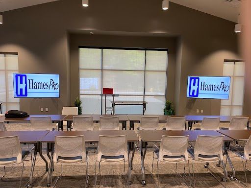 Conference room with rows of chairs facing a stage and two presentation screens.