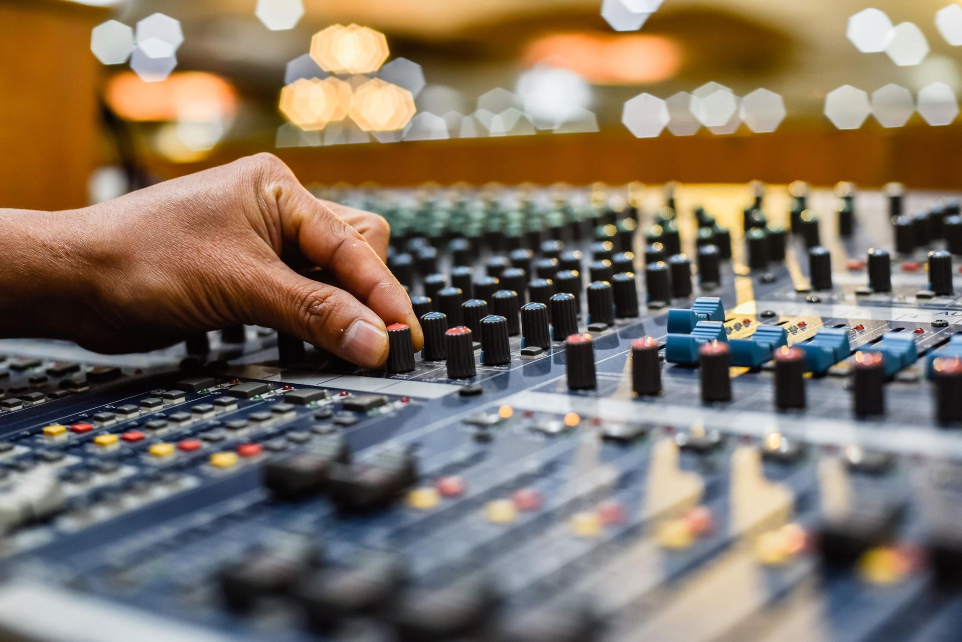 Hand adjusting knobs on an audio mixing console in a studio.