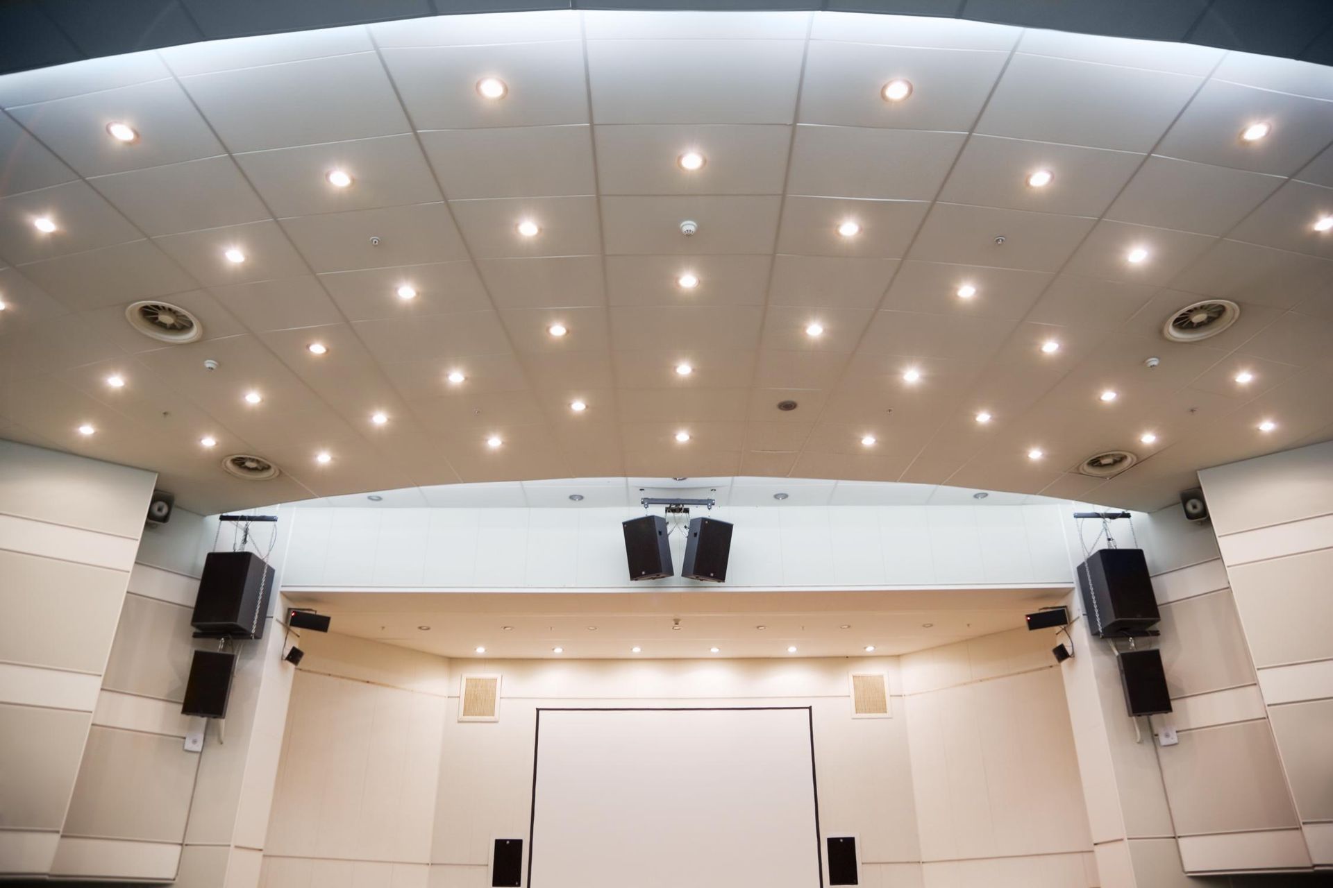Empty modern auditorium with recessed ceiling lights and a projection screen at the front
