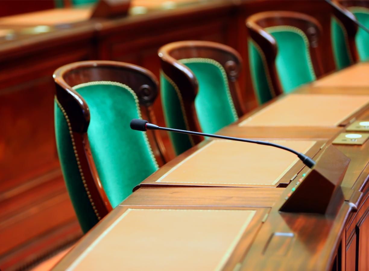 Empty conference room chairs with teal backs and microphones along a wooden meeting table