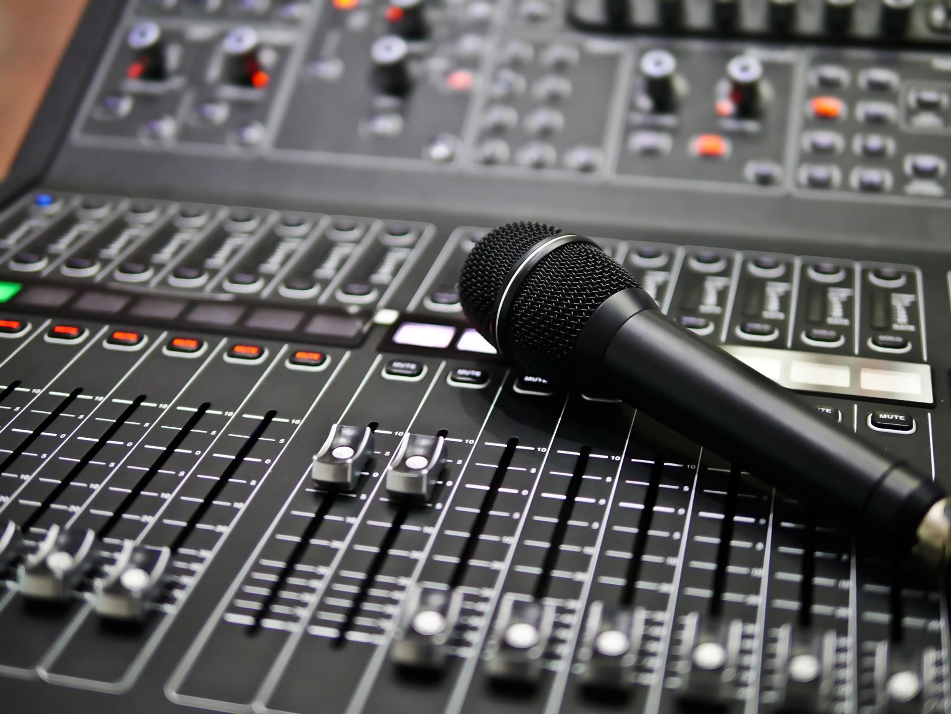 Microphone resting on an audio mixing console with sliders and knobs