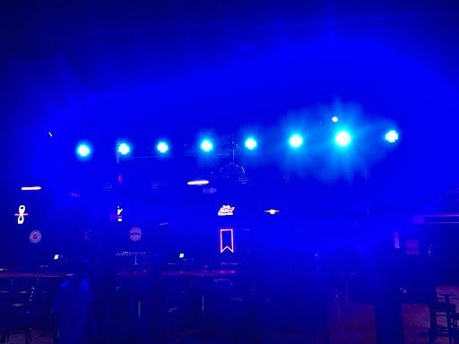 Blue stage lights over a dark concert stage with silhouetted equipment and signs