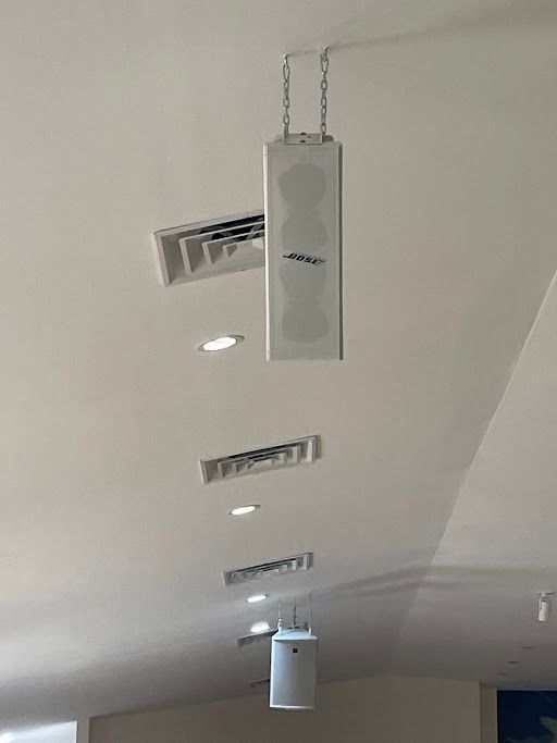 Ceiling with recessed lights, air vents, and hanging rectangular speakers in a hallway