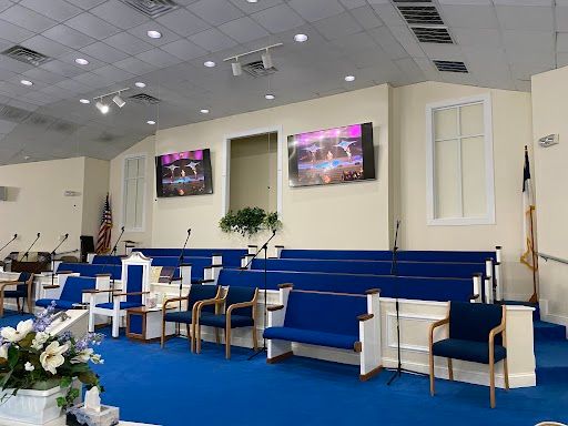 Church sanctuary with blue carpet, white chairs, floral arrangements, and two wall-mounted screens