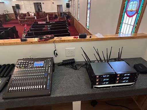 Audio mixing console overlooking a church sanctuary with pews and stained-glass windows