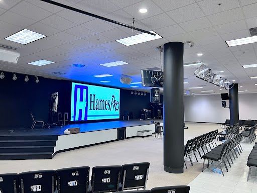 Empty church auditorium with stage, blue-lit screen, black chairs, and large columns