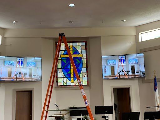 A red ladder stands in a church sanctuary beneath a colorful stained-glass window.