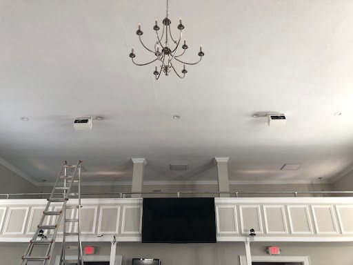 Indoor hall with white ceiling, chandelier, wall panels, and a ladder leaning on the left.