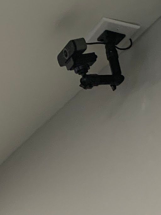 Ceiling-mounted security camera on a white wall, angled toward the room.