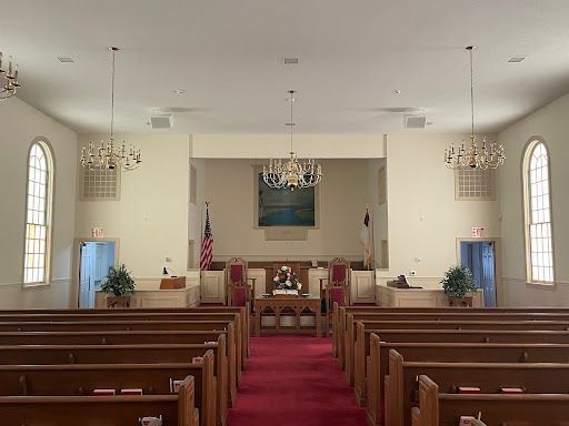 Empty church sanctuary with wooden pews, red carpet aisle, chandeliers, and arched windows