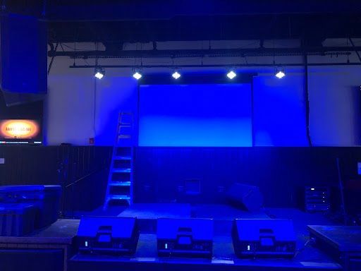 Blue-lit empty stage with stairs, overhead spotlights, and speakers in front