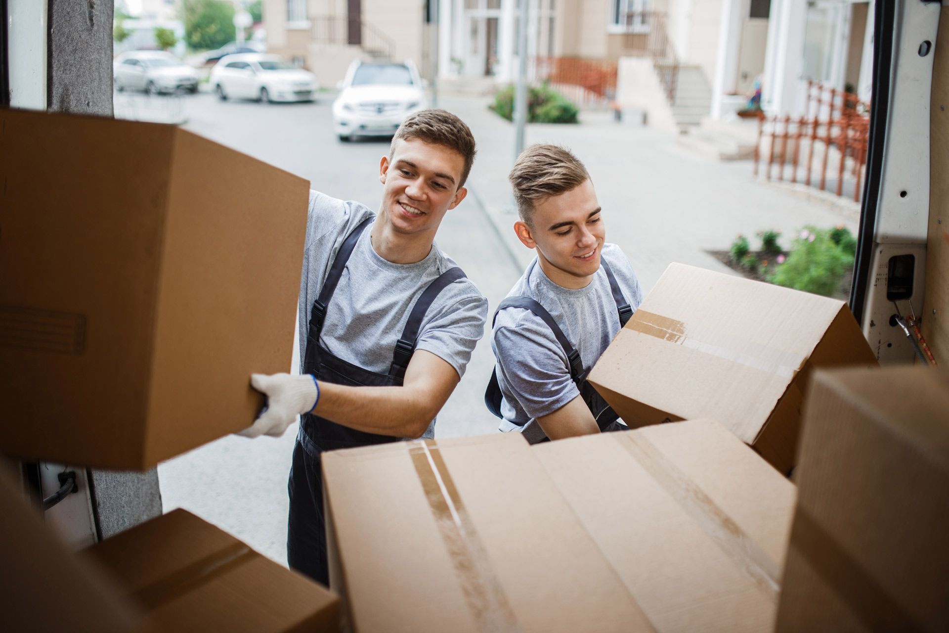 Two movers loading boxes into a truck, smiling, outdoors.