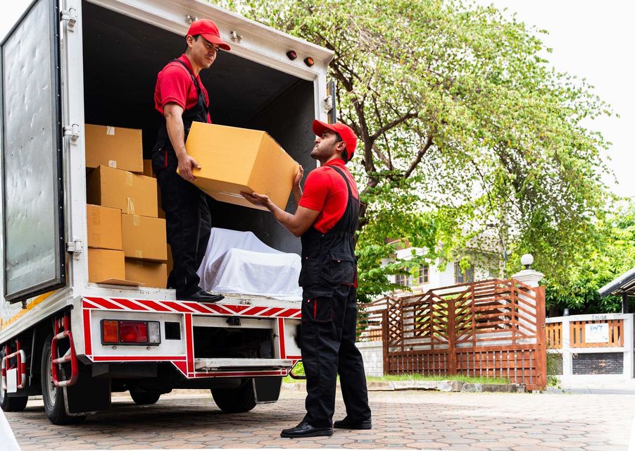 Two movers in red shirts and caps load boxes into a truck.