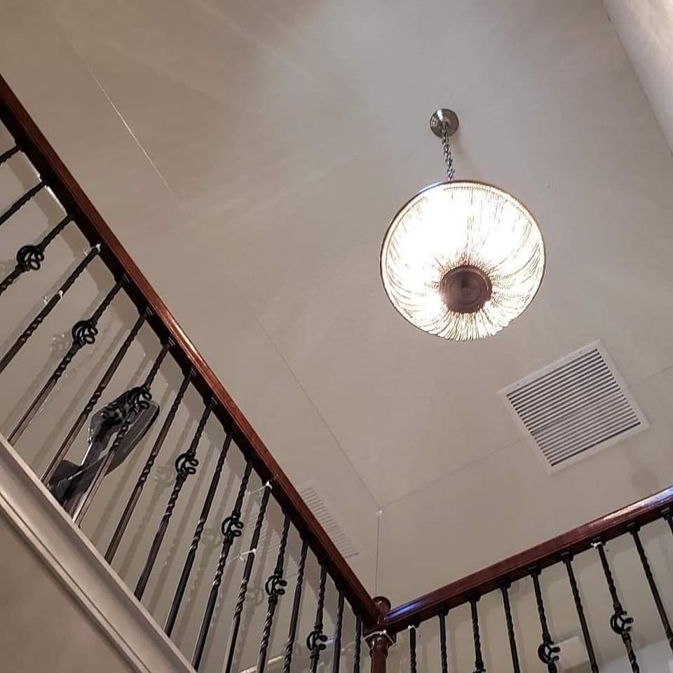 Staircase with dark railing and brown handrail. A round, ornate light fixture hangs from the ceiling.