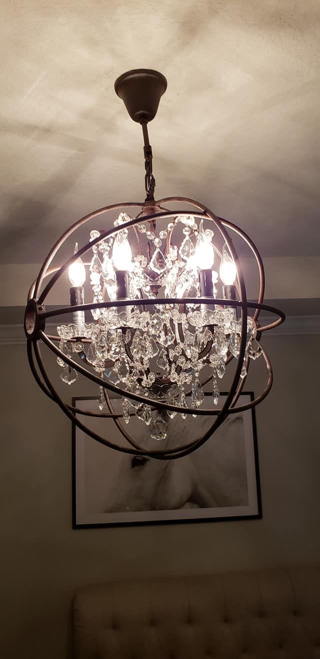 Chandelier with crystal accents and dark metal frame, hanging over a framed artwork.