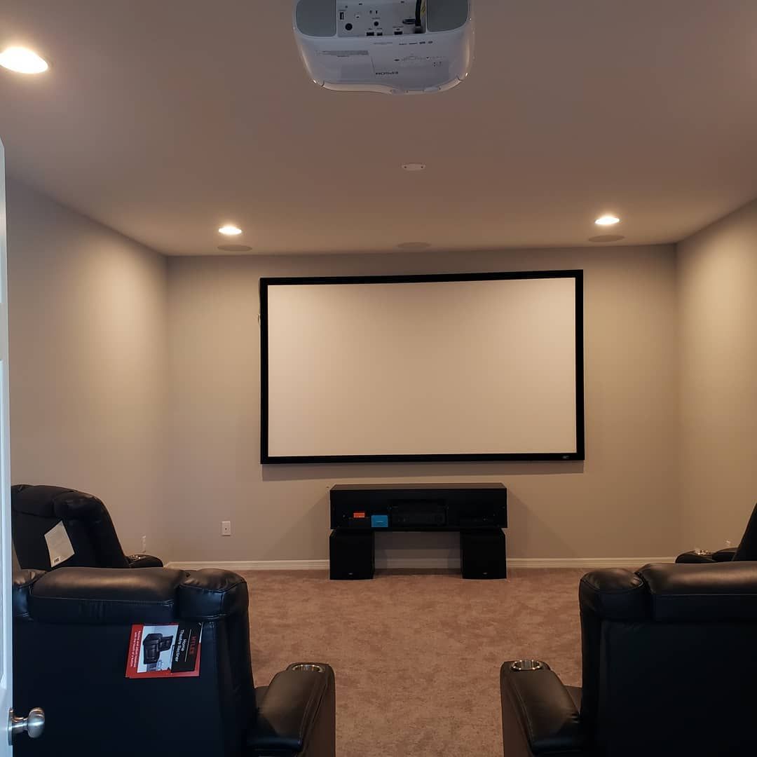 Home theater room with projector, screen, and black recliners. Beige walls, brown carpet.