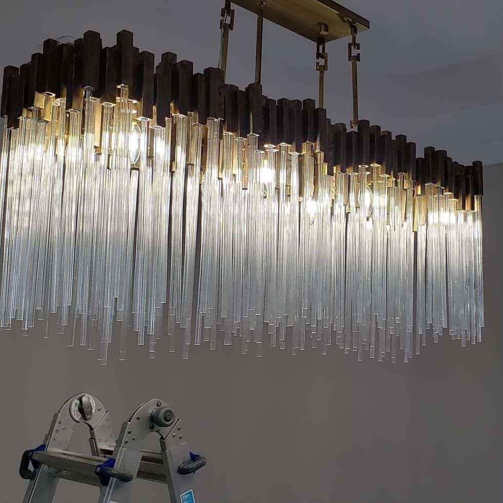 Rectangular chandelier with clear glass rods and gold accents, hanging above a stepladder.