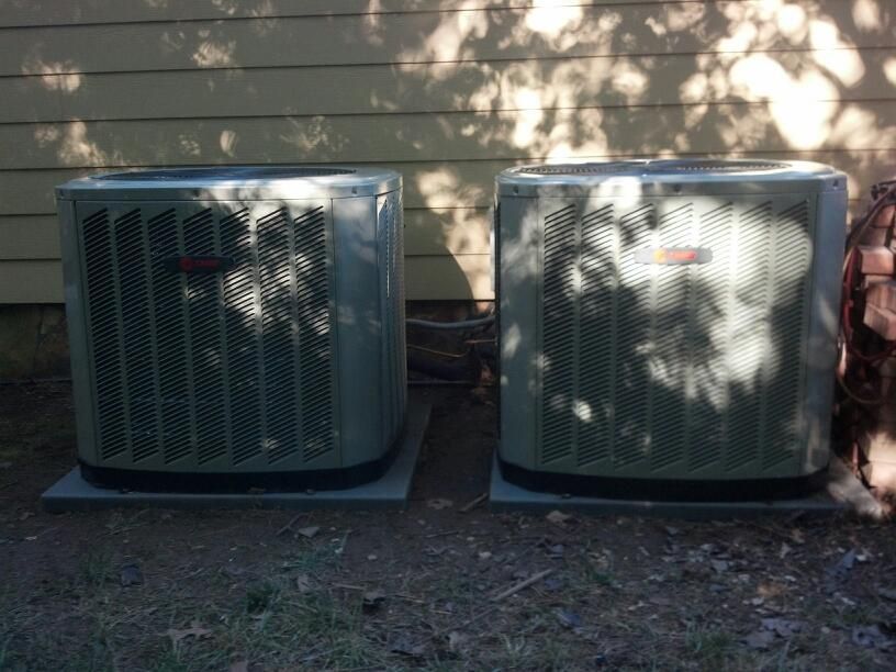 Two gray air conditioning units sitting on concrete pads outside a building.