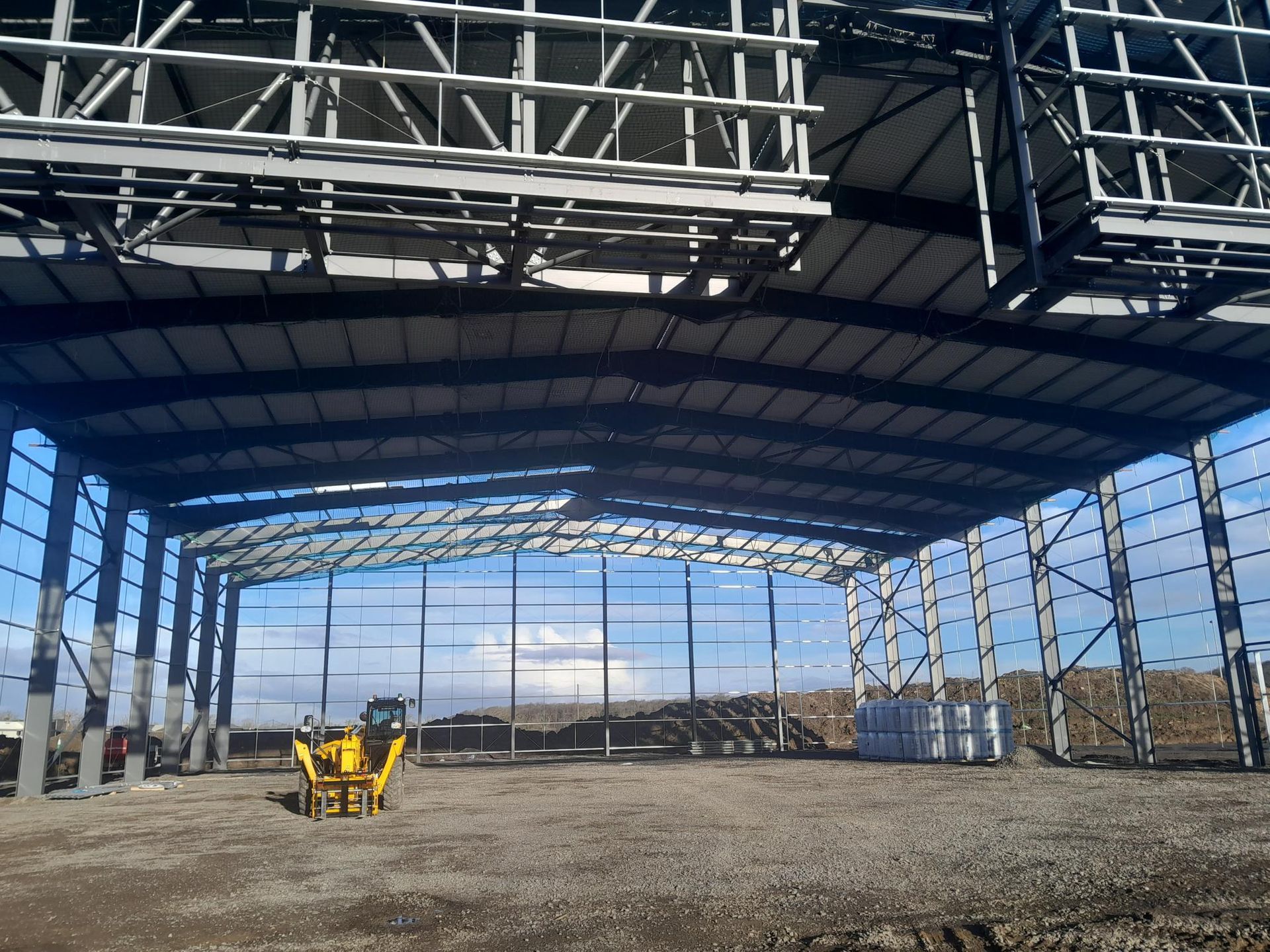 A yellow tractor is parked under a large metal structure