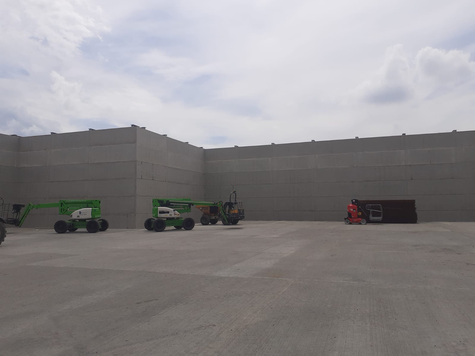 A row of green vehicles are parked in front of a large concrete wall.