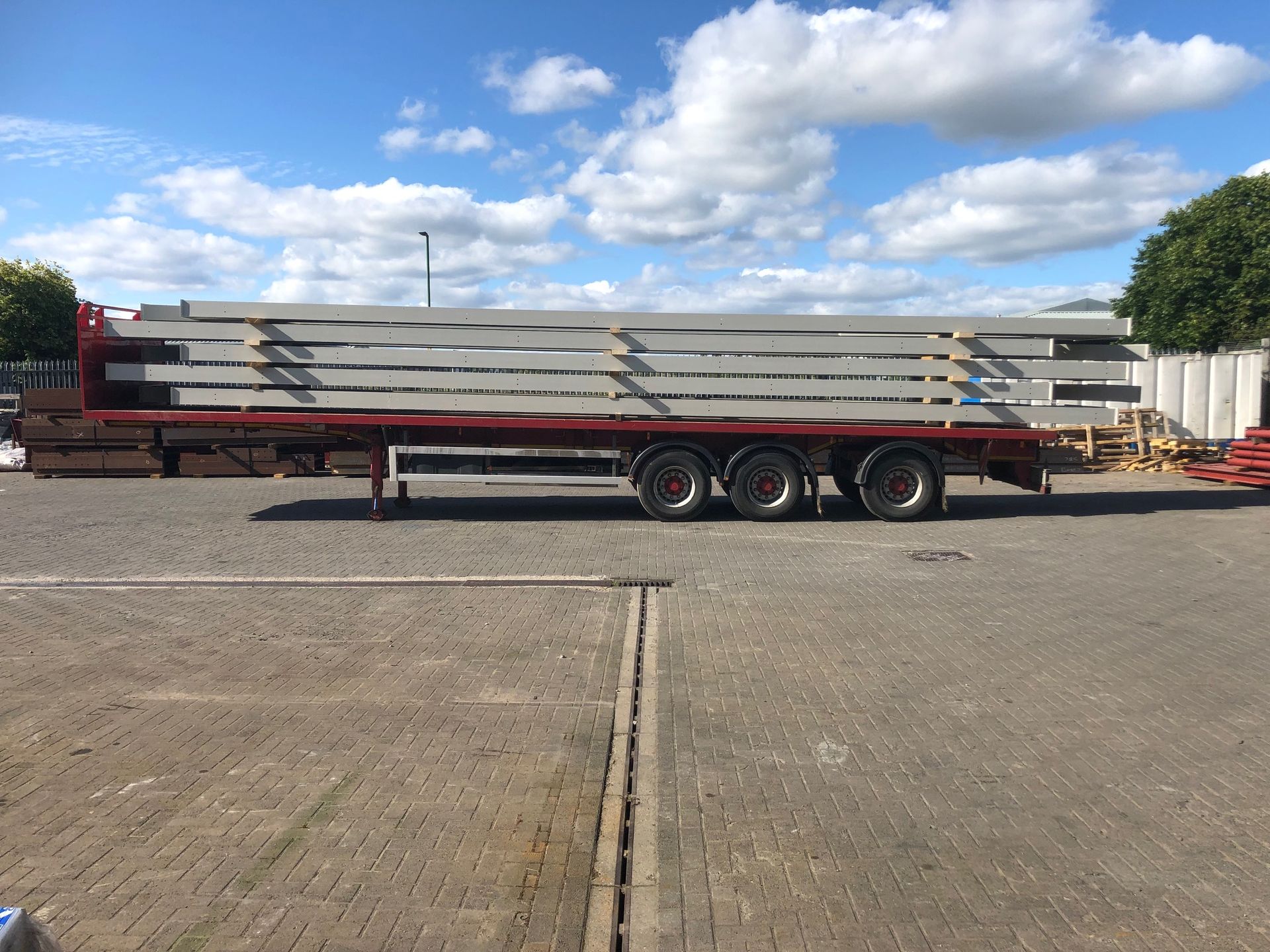 A red semi truck is carrying a stack of concrete beams.