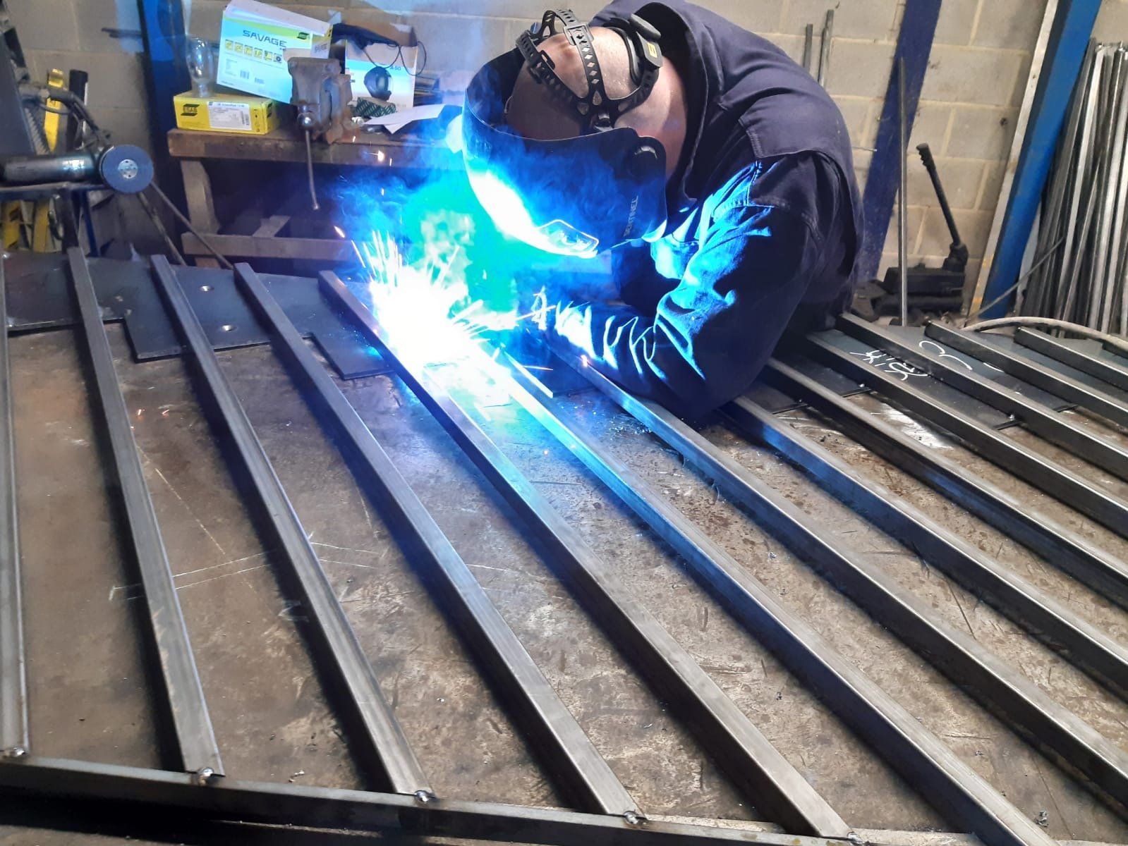 A man wearing a welding mask is welding a piece of metal