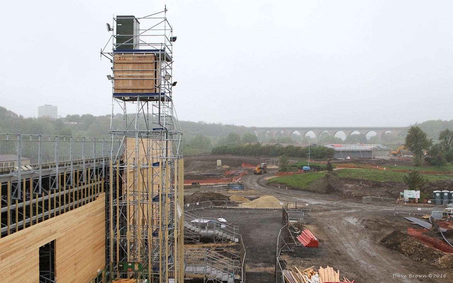 A construction site with scaffolding and a bridge in the background.