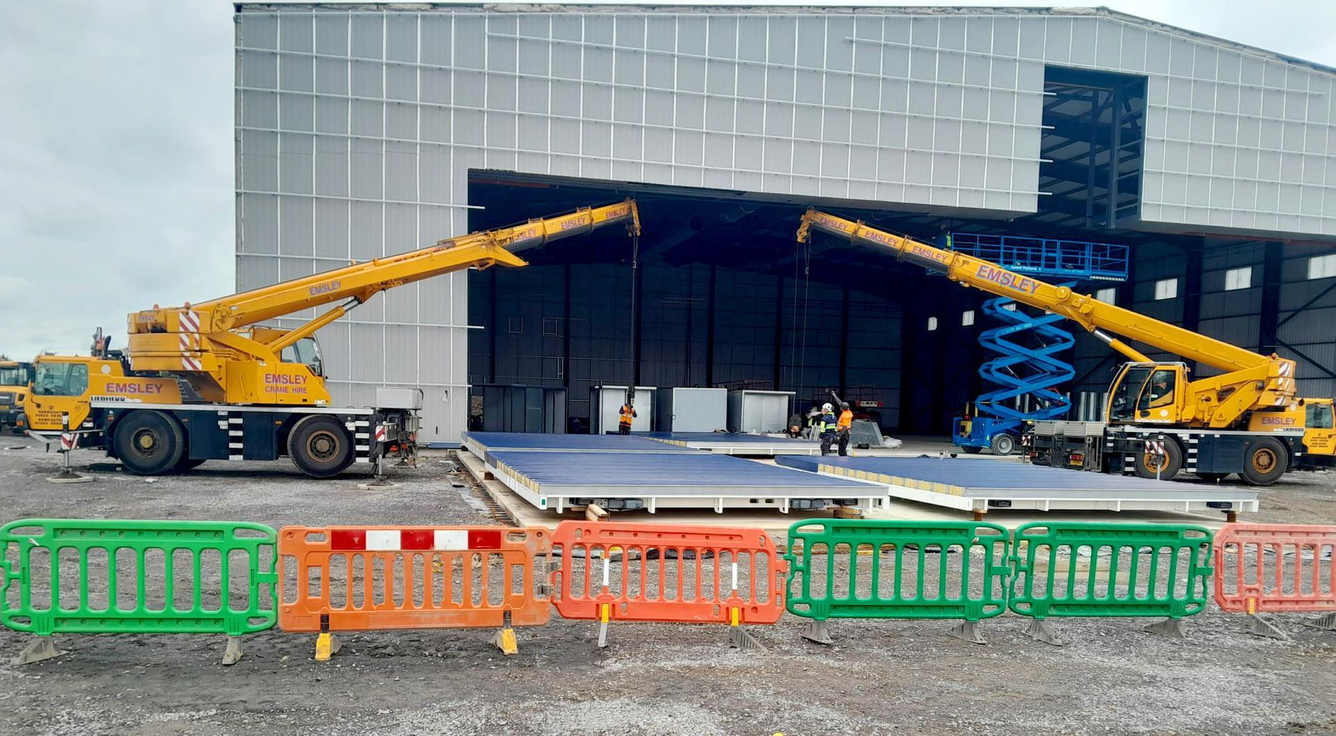 Two crane trucks are parked in front of a large building.
