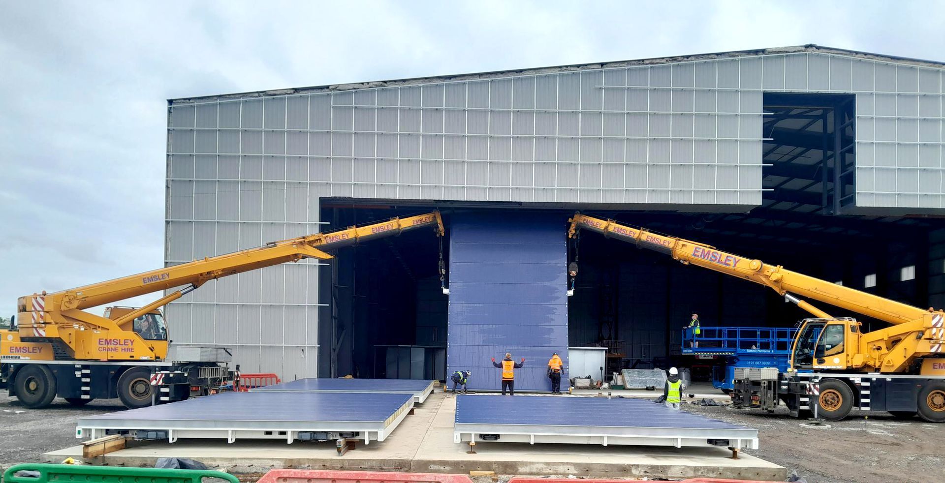 A couple of cranes are sitting in front of a hangar.