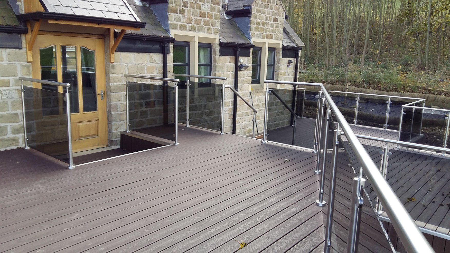 A wooden deck with a stainless steel railing in front of a brick building.