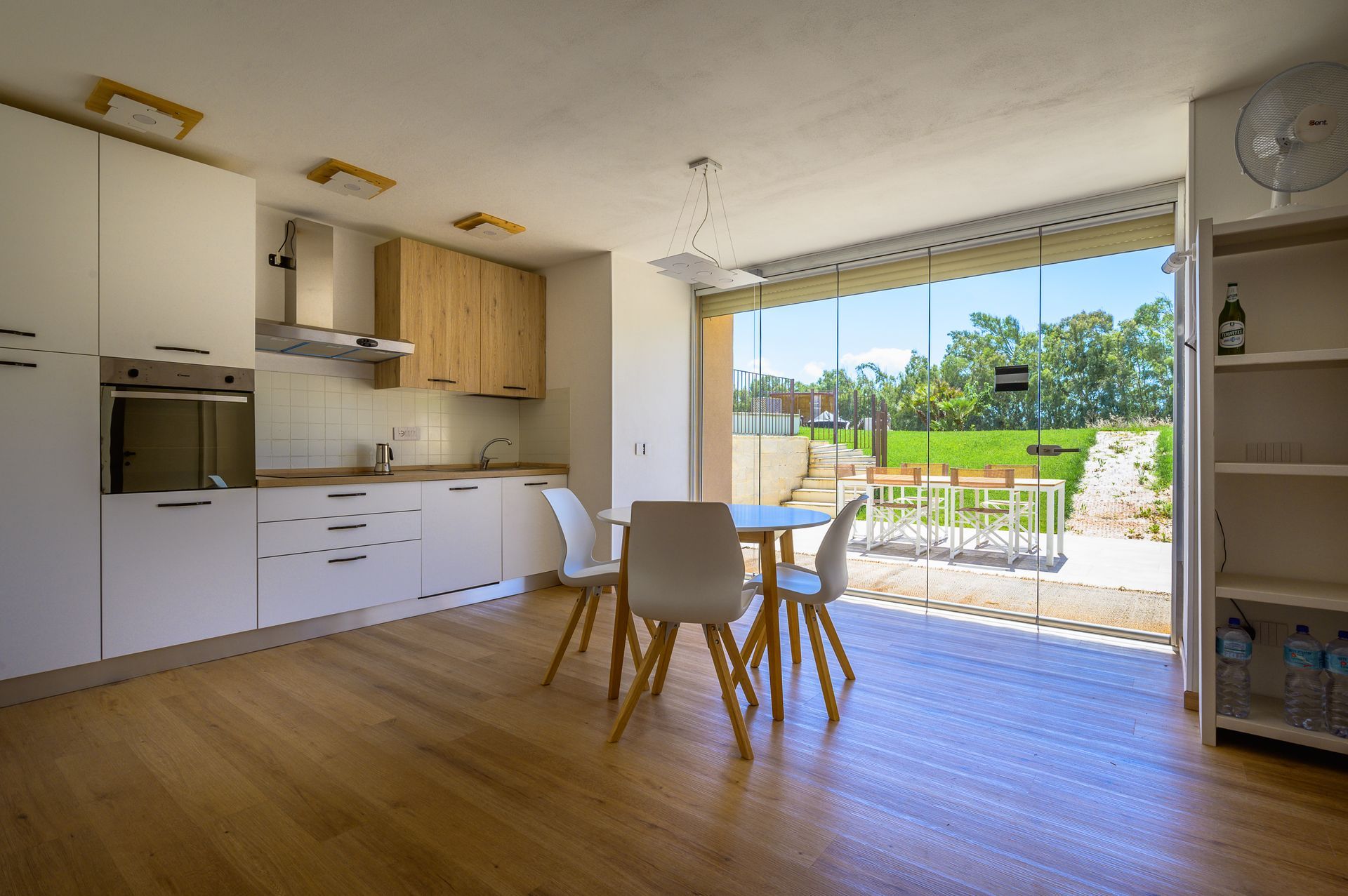 Cucina luminosa con mobili bianchi, dettagli in legno, tavolo da pranzo e grandi porte in vetro che si aprono su un patio.
