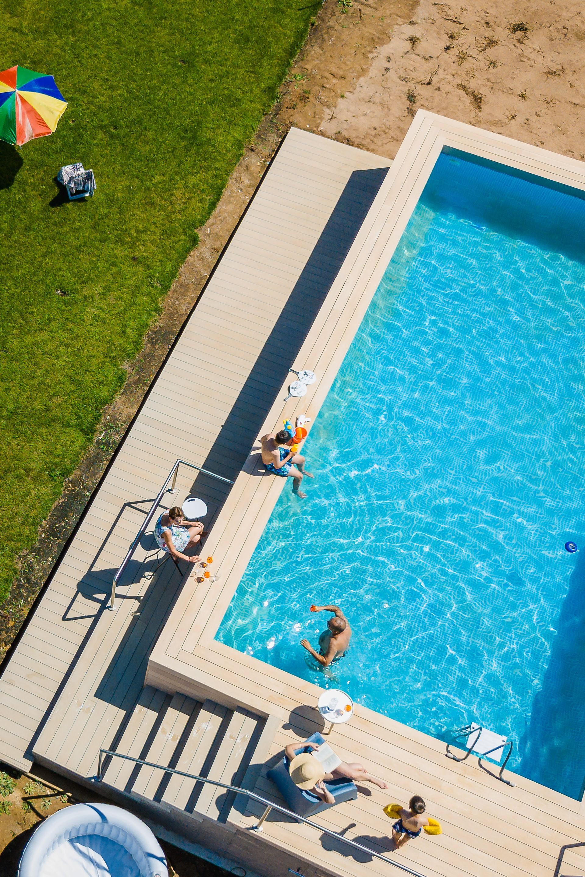 Persone che si rilassano a bordo piscina in una giornata di sole.