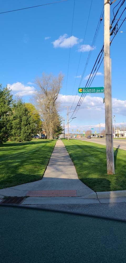 A Sidewalk Leading to a Grassy Field With a Street Sign.