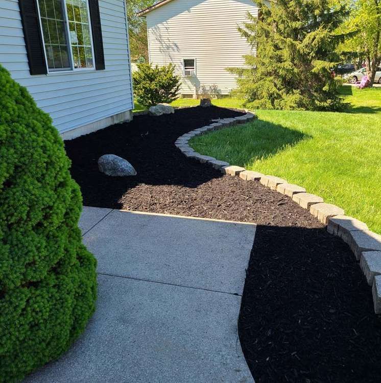 A Concrete Walkway Leading to a House With Black Mulch
