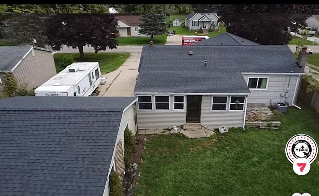 Aerial view of a house with dark gray roof, white siding, and a camper parked in the driveway.