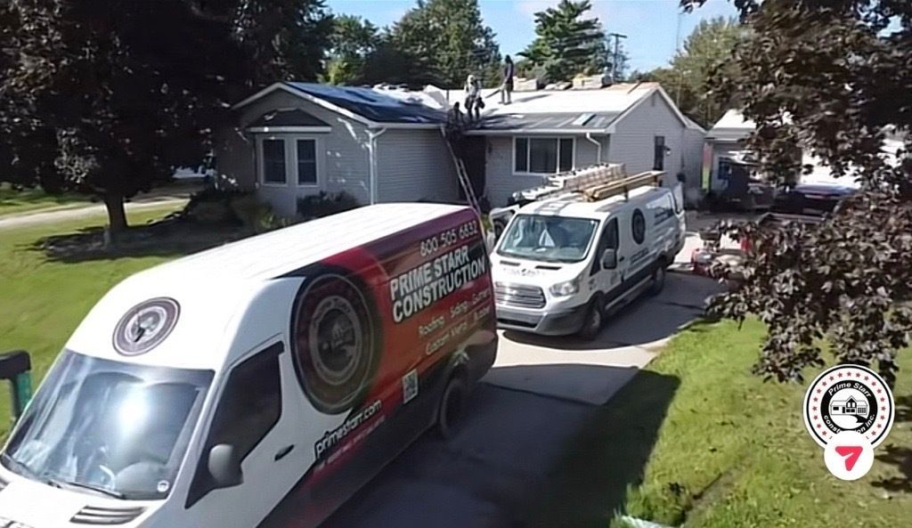 Two white service vans parked in a driveway beside a small house on a sunny day