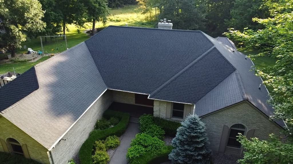 An aerial view of a house with a black roof surrounded by trees.