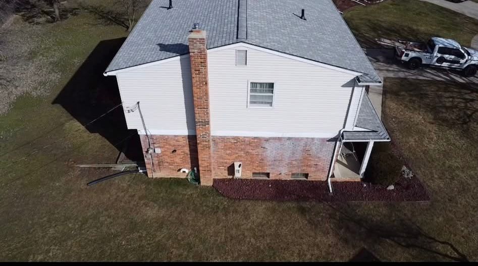 An aerial view of a house with a gray roof and a chimney. An aerial view of a house with a gray roof and a chimney.