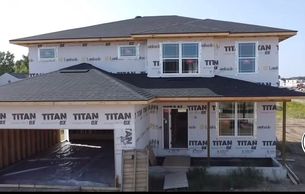 Partially built two-story house wrapped in Tyvek with unfinished roof and garage opening