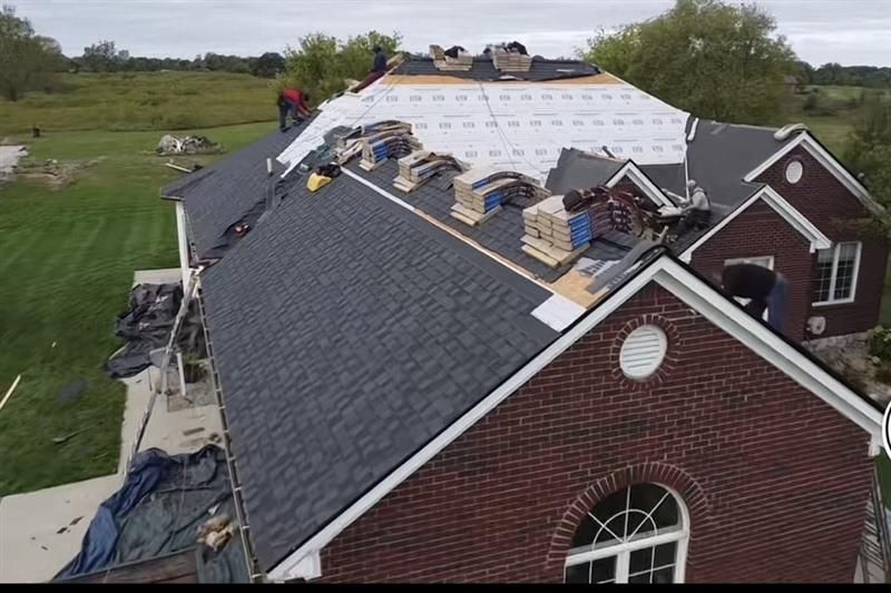 Roofers repairing a dark shingled church roof with materials stacked along the ridge
