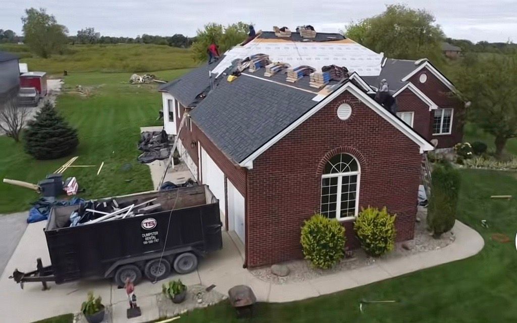 Red brick house with workers repairing a roof and a dumpster in the driveway