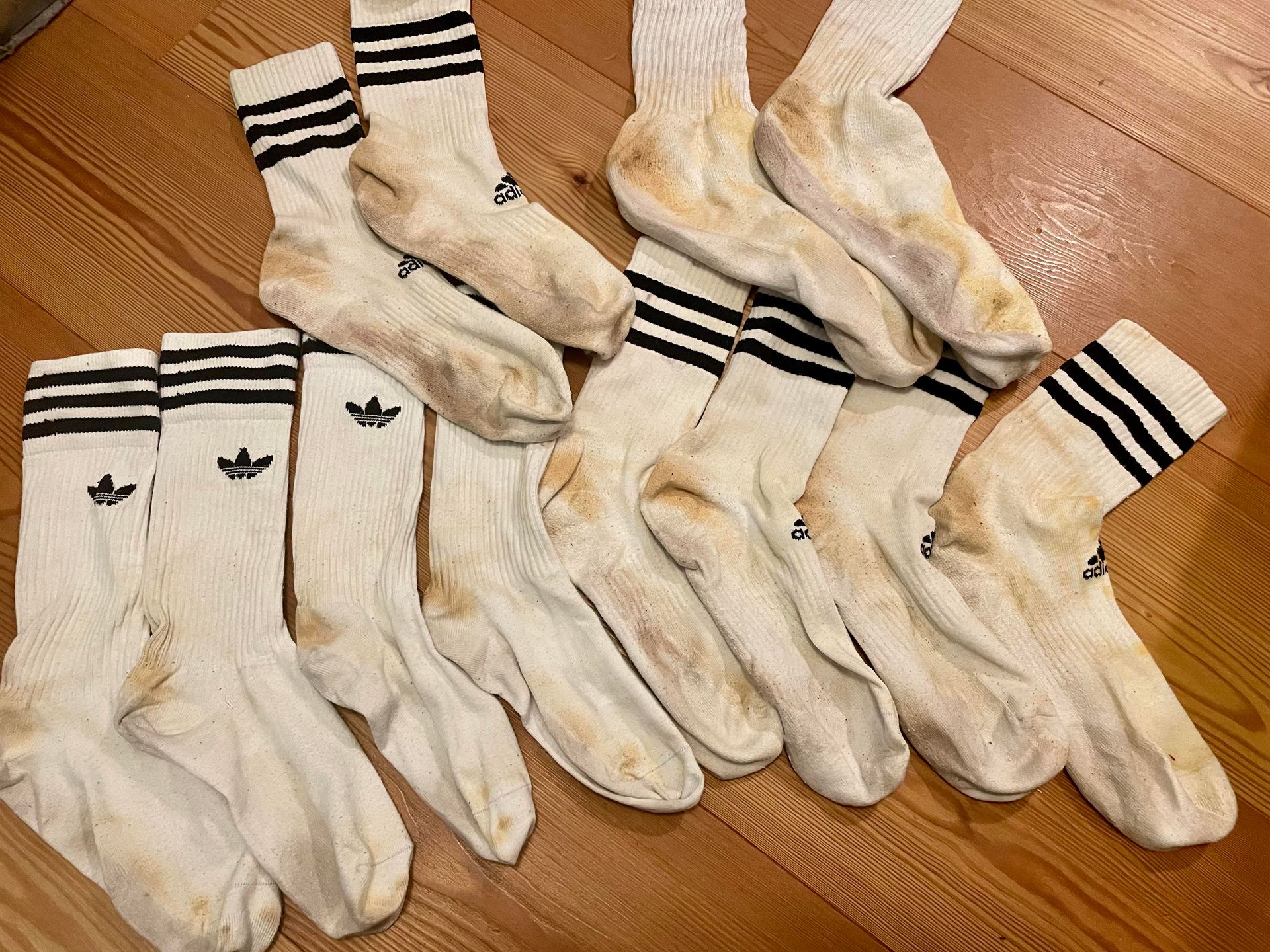 Meerdere paren witte Adidas-sokken met zwarte strepen, vuil en versleten.
