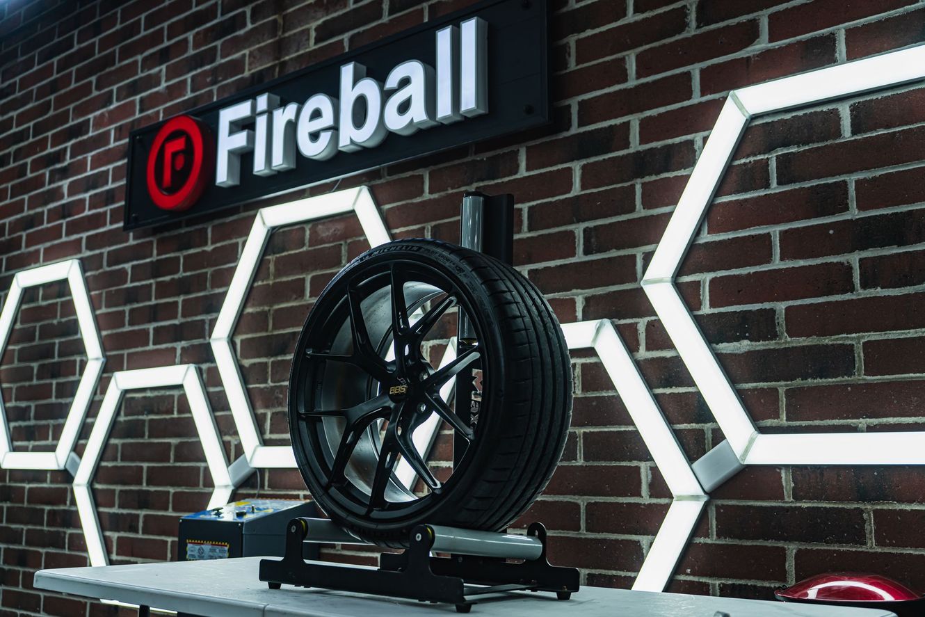 A car tire on a stand inside a shop with a Fireball sign on a brick wall.